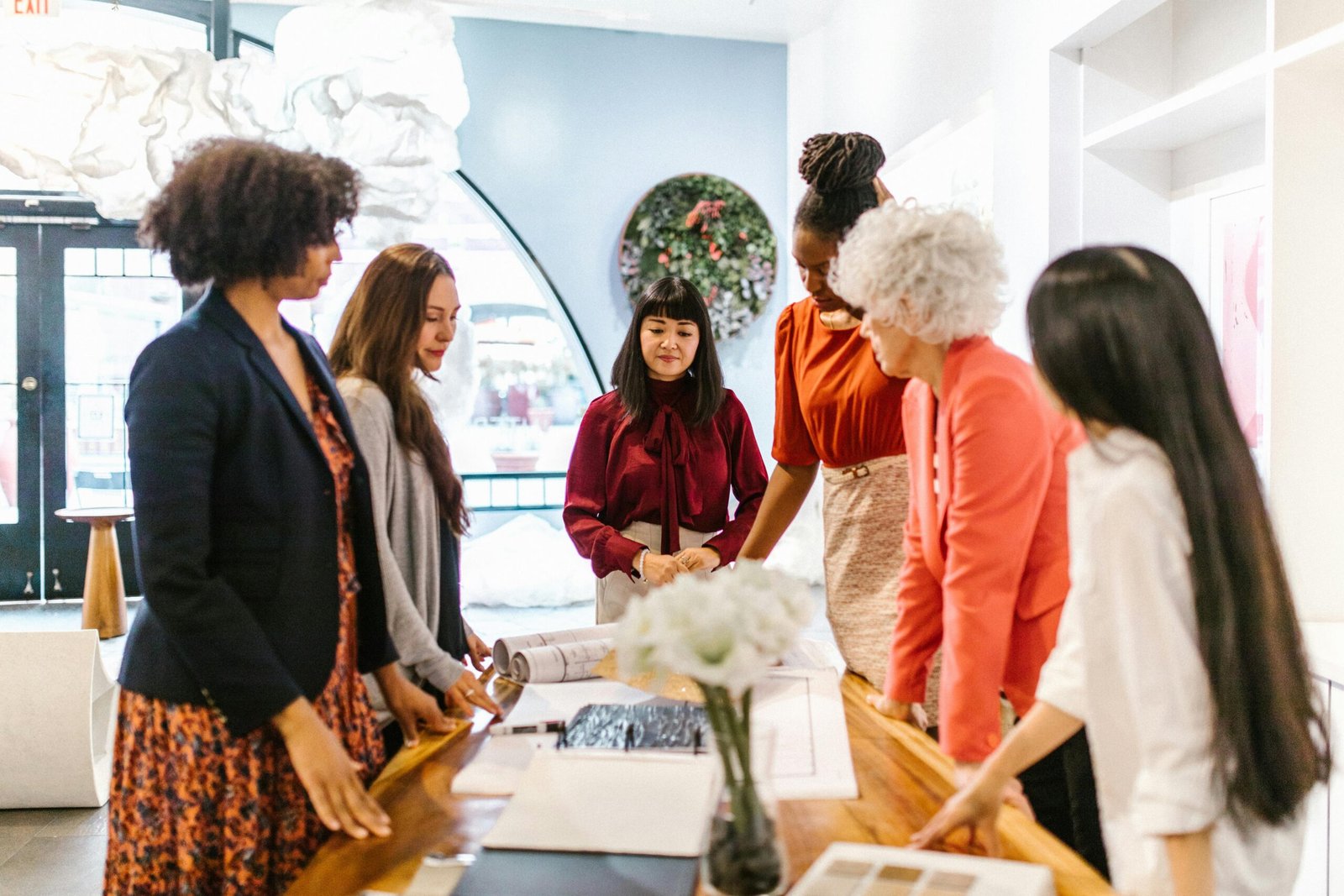 A diverse group of women engage in a business meeting in a creative modern office setting.